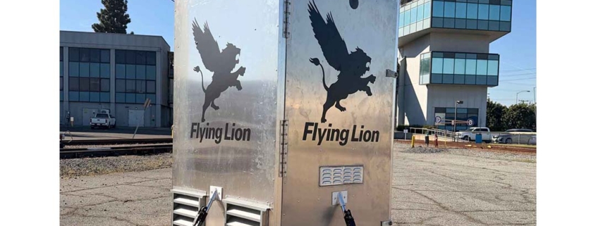 Alt Text: Flying Lion DroneBooth™ with Hex Universal Dock mounted on top, shown at an airfield with an air traffic control tower in the background