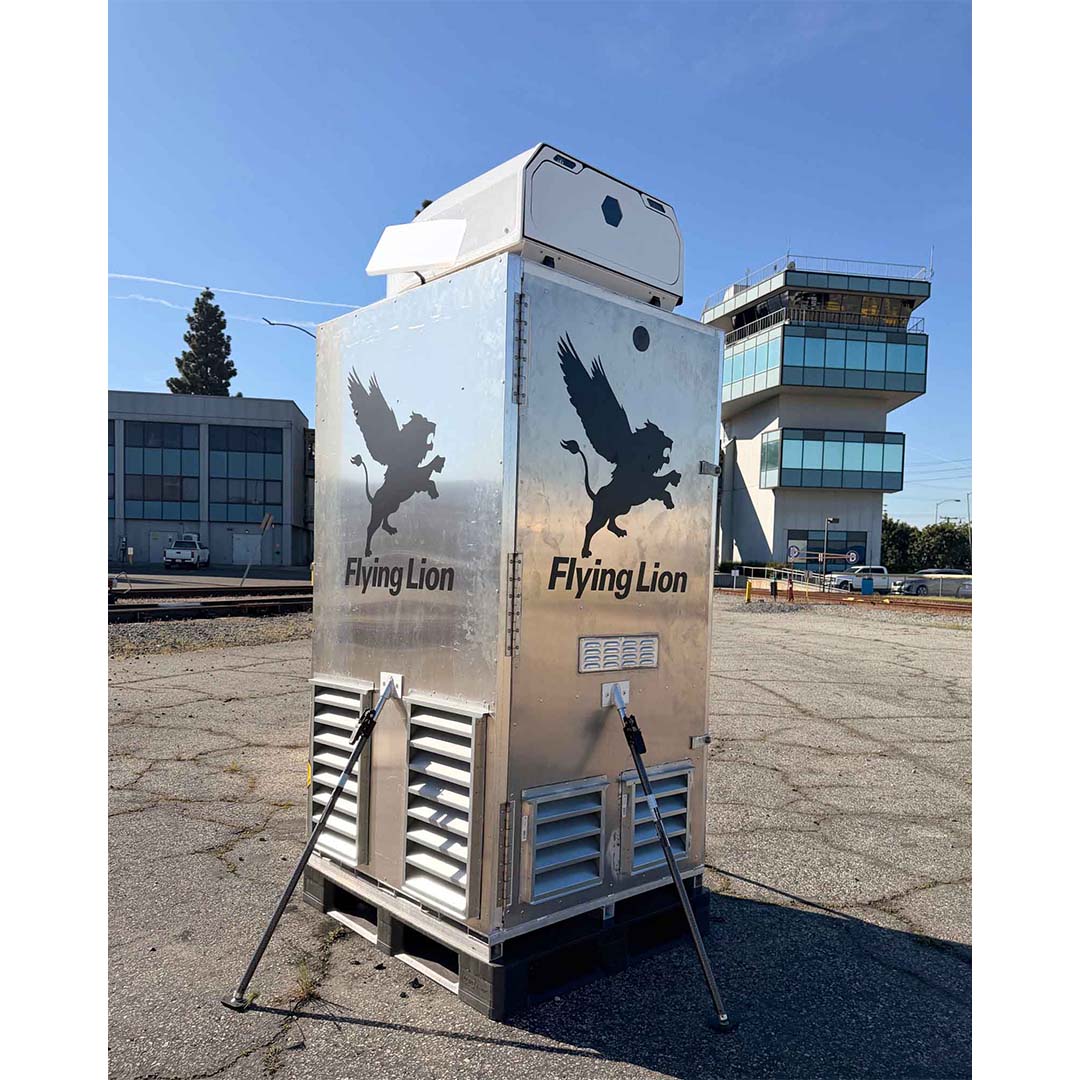 Flying Lion DroneBooth™ with Hex Universal Dock — Airfield Deployment Alt Text: Flying Lion DroneBooth™ with Hex Universal Dock mounted on top, shown at an airfield with an air traffic control tower in the background
