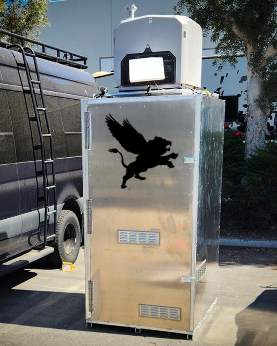 Flying Lion DroneBooth™ — Rapidly Deployable Drone Dock Flying Lion DroneBooth™ drone dock enclosure with Flying Lion logo decal, shown next to a van in a parking area