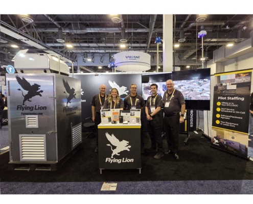 Flying Lion team at their ISC West trade show booth showcasing the DroneBooth™ rapid-deploy drone dock enclosure alongside pilot staffing services signage.